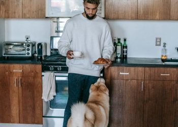 Black man standing with cup of coffee and croissant near Akita Inu